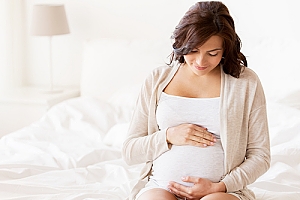 Pregnant woman sitting on bed with hands on belly