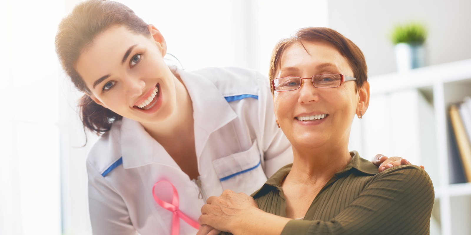 Female patient with a doctor wearing pink ribbon for breast cancer awareness in medical office.