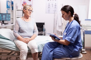 Nurse Practitioner writing prescription on clipboard discussing with senior man