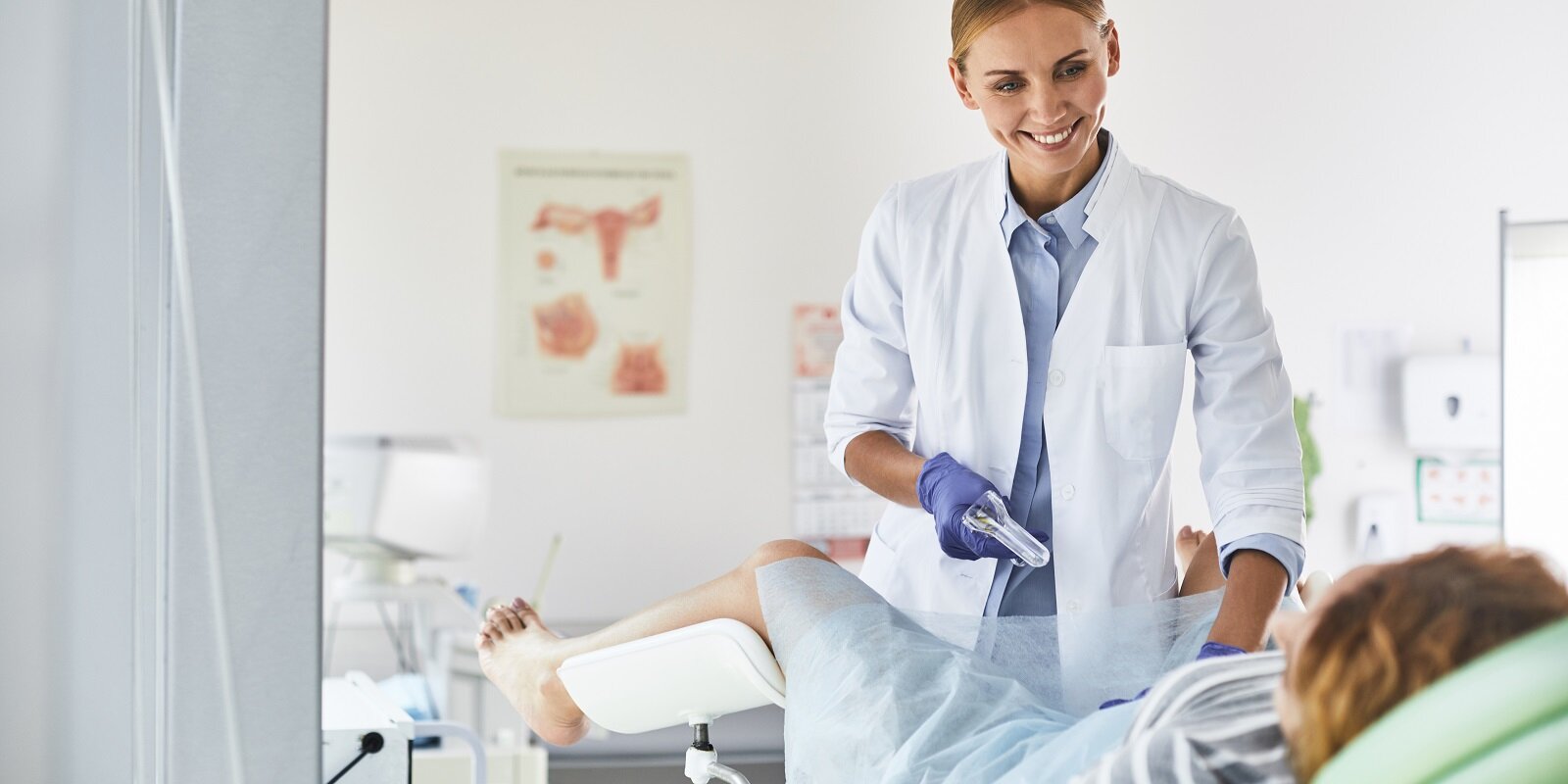 gynecologist in white lab coat and sterile gloves using vaginal speculum during pelvic exam