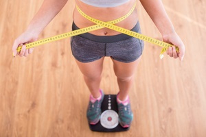 pretty slim woman with measure around her body is standing on the scales