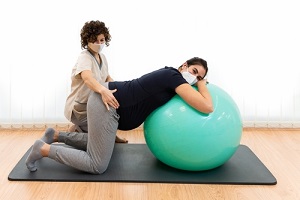 pregnant woman doing pilates exercises with a ball with the help of her physiotherapist