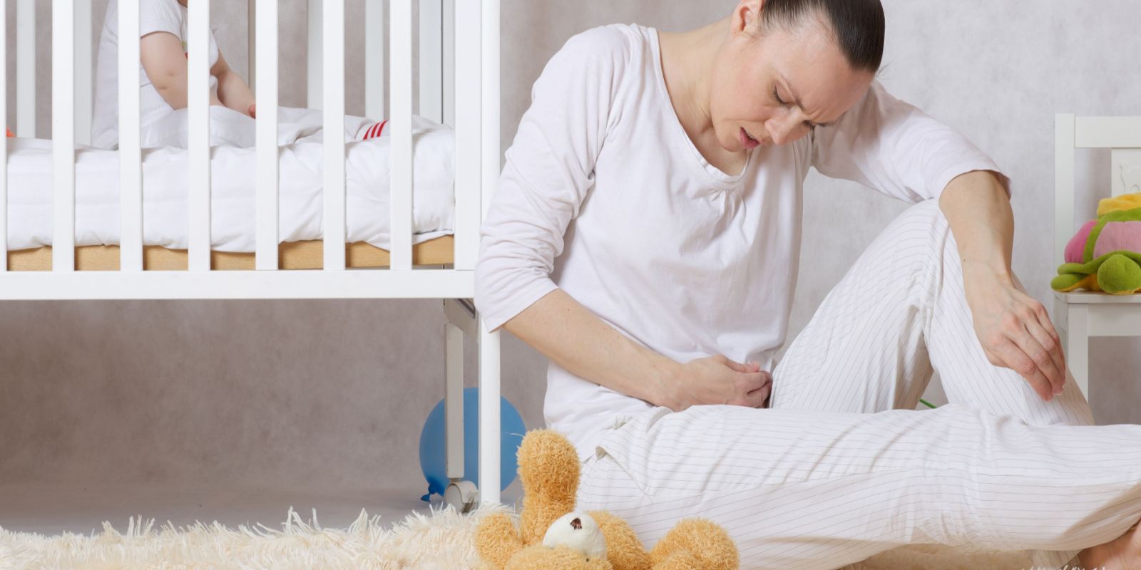 A woman is experiencing postpartum pain and stress while sitting beside a baby bed