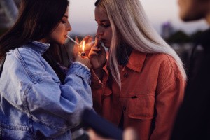 Two women light cigarettes together