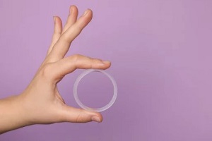 women hand holding vaginal ring in front of purple background