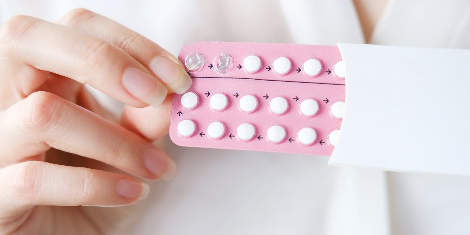 unrecognized woman in white blouse holding hormonal oral contraceptives in a pink blister