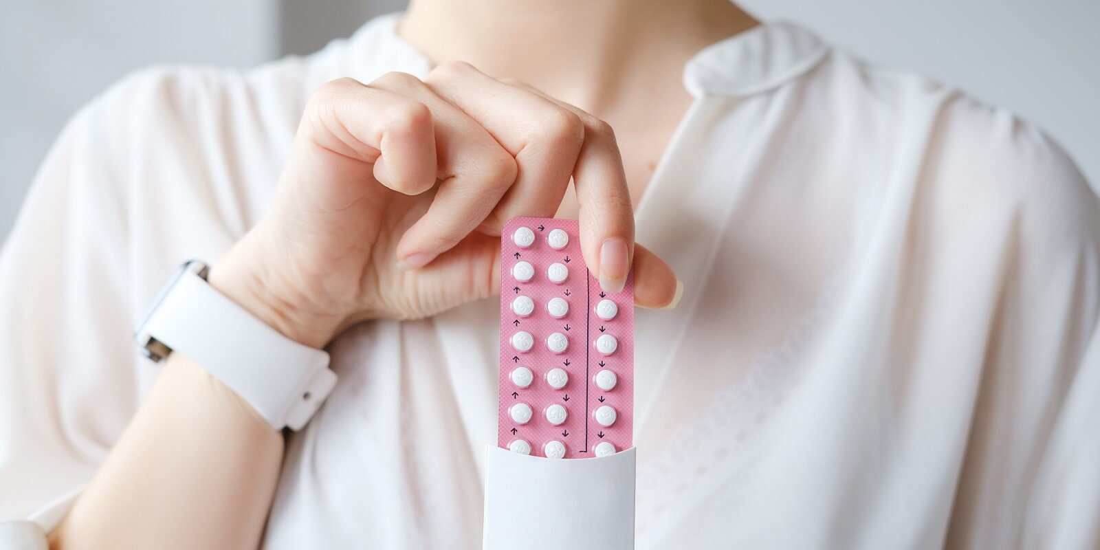 woman in white blouse holding hormonal oral contraceptives in a pink blister