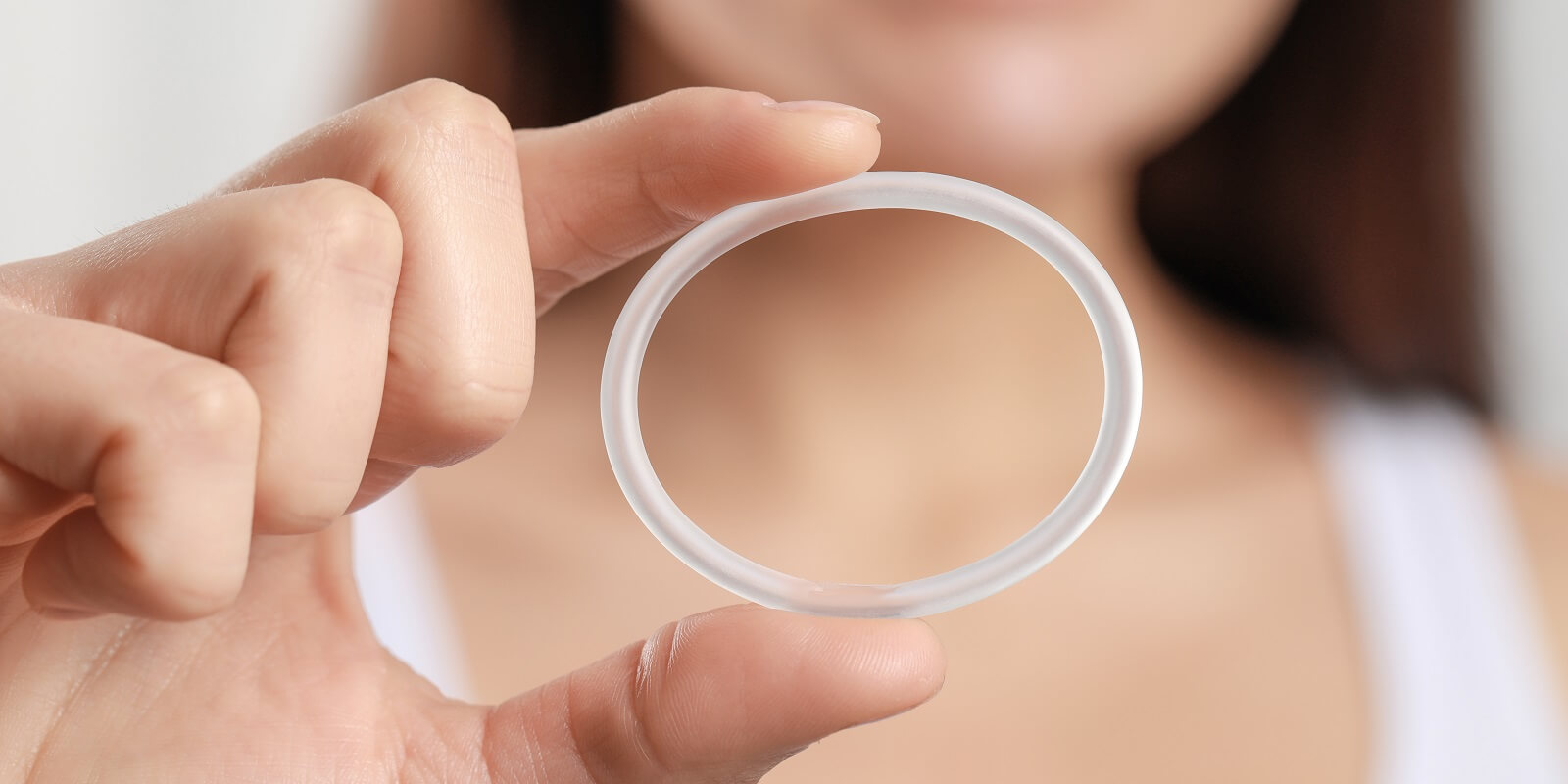woman holding diaphragm vaginal contraceptive ring on blurred background