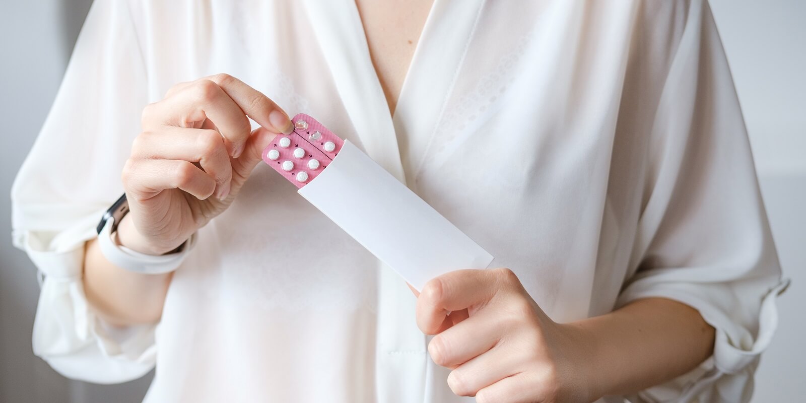 woman in white blouse holding hormonal oral contraceptives in a pink blister