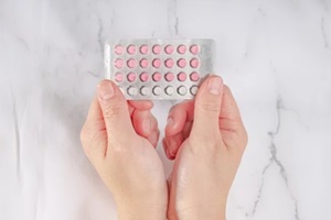 female hands holding birth control pills on a marble background