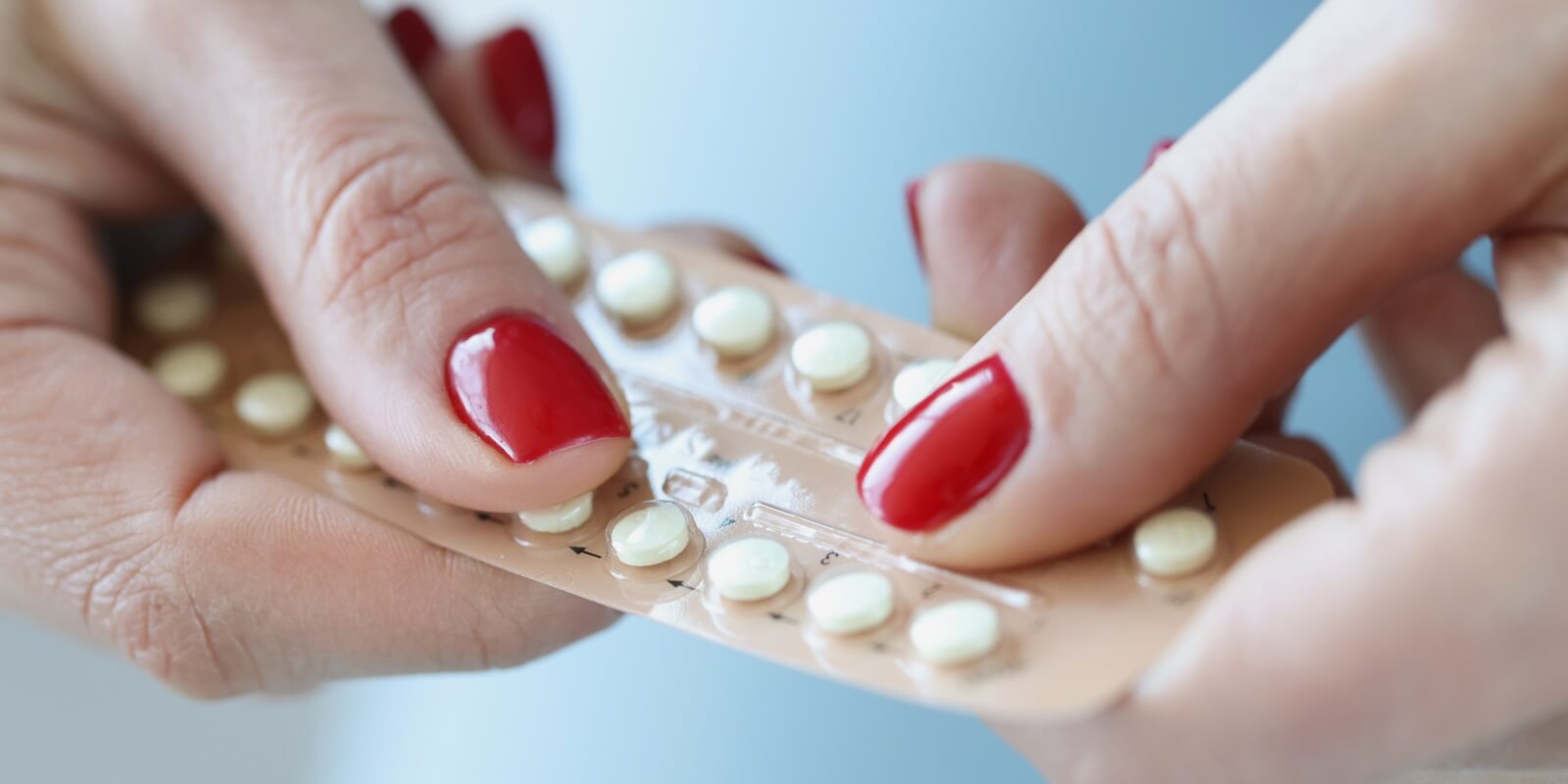 Raleigh, NC woman with red manicure holding blister with contraceptive hormonal pills in her hands closeup