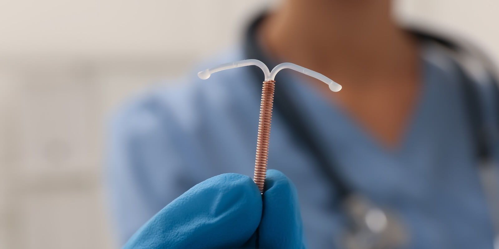 doctor holding T-shaped intrauterine uterine device (IUD) birth control device on blurred background