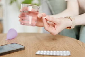 side view closeup of young woman taking birth control pills with glass of water