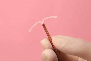 doctor holding T-shaped intrauterine birth control device on pink background