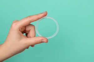 woman holding diaphragm vaginal contraceptive ring on turquoise background, closeup