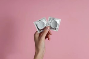 female hand holding condom on pink background