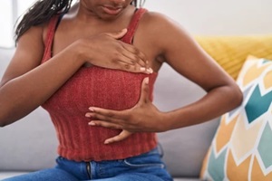 african american woman examining breast with hand sitting on sofa at home