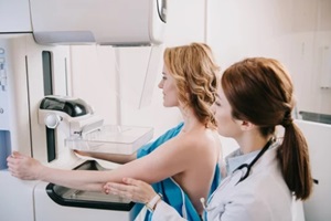 young radiographer standing near patient while making mammography test on x-ray machine