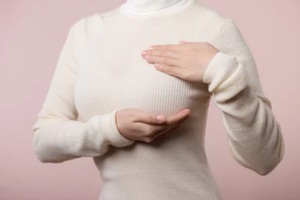 woman hands checking lumps on her breast for signs of breast cancer on pink background