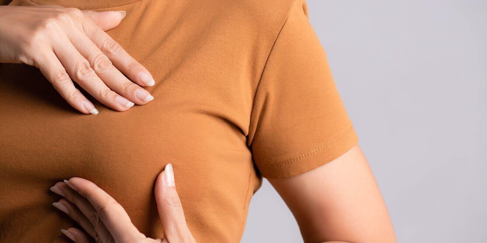 woman hand checking lumps on her breast for signs of breast cancer on gray background