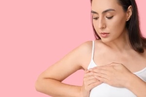 young woman checking her breast on pink background with space for text