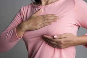 woman hand checking lumps on her breast for signs of breast cancer on gray background. Healthcare concept