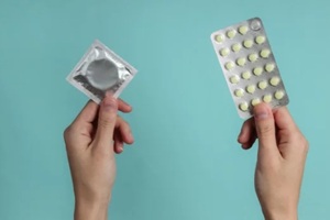 women holding condom and birth control pills in both hands