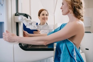 smiling radiologist standing near patient while making mammography diagnostics on x-ray machine