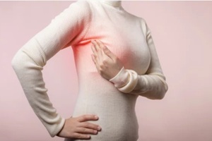 woman hands checking lumps on her breast for signs of breast cancer on pink background