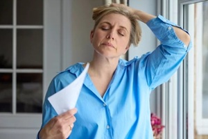 menopausal mature woman having hot flush at home cooling herself with letters or documents in Raleigh, NC
