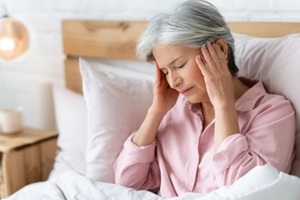 woman suffering from headache, touching temples, menopause lying in bed at home