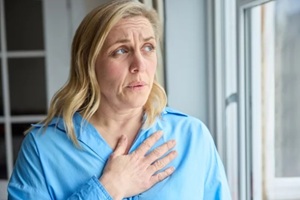 menopausal mature woman at home standing by window suffering with heart palpitations
