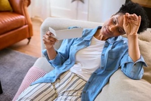 menopausal mature woman sitting on sofa at home having hot flush fanning herself