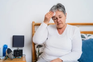 senior woman experiencing hot flashes or fever, using cotton pad to wipe sweat from forehead while sitting on bed - doctors who specialize in menopause