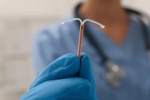 doctor holding T-shaped intrauterine birth control device on blurred background