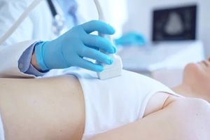 man, wearing blue medical gloves, is using ultrasound machine to examine internal organs of a patient woman