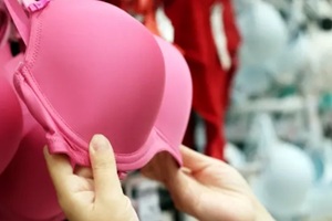 woman chooses pink support bra hanging on rack in lingerie store