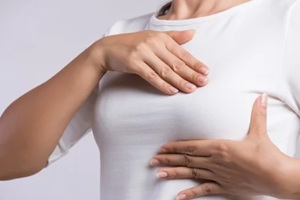 woman hand checking lumps on her breast for signs of breast cancer on gray background