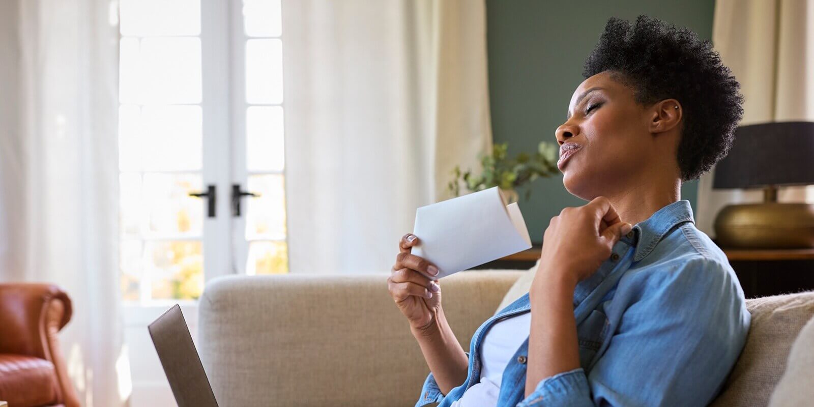 menopausal mature woman at home with laptop having hot flush fanning herself