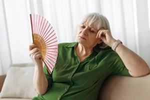 senior woman cooling herself with handheld fan at home living room