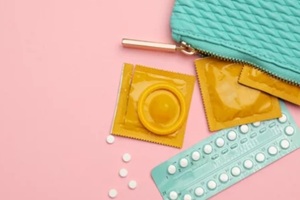 condoms and birth control pills in purse on pink background