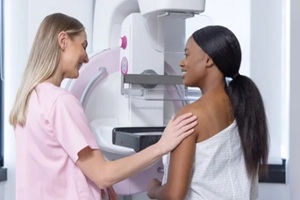 female tech in pink scrubs guiding African-American woman undergoing mammography with clear paddle