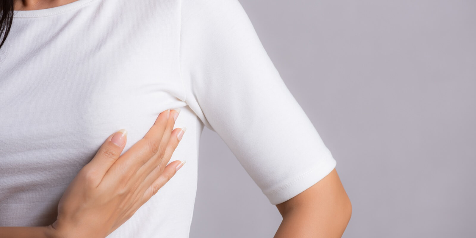 woman hand checking lumps on her breast for signs of breast cancer on gray background